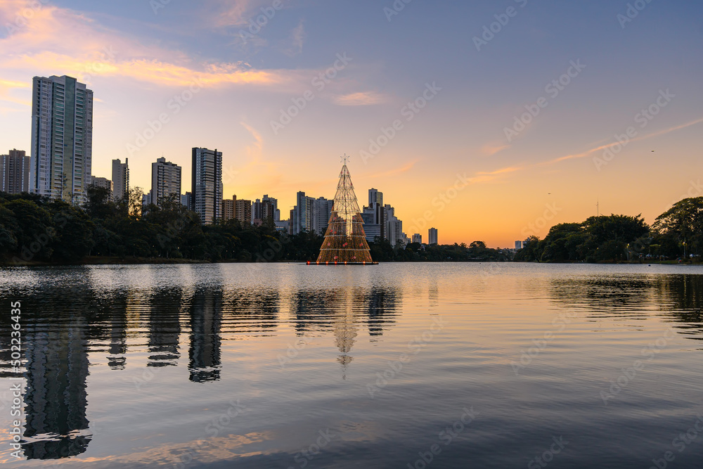 Igapo lake at sunset during christmas, Londrina - PR, Brazil. Beautiful city lake with christmas tree shining in the middle of the lake and the city buildings on background.