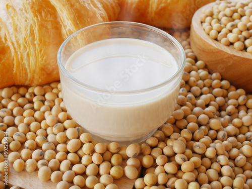 Glass of hot soy milk on lots of soy beans with wooden bowl of soy beans with some croissants 