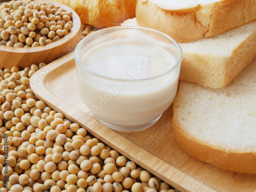 Delicious soy milk and some breads on wooden tray and lots of soy beans with wooden bowl of soy beans and  some croissant