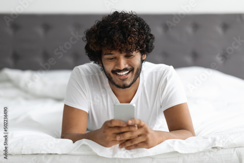 Portrait of handsome hindu guy laying on bed with phone