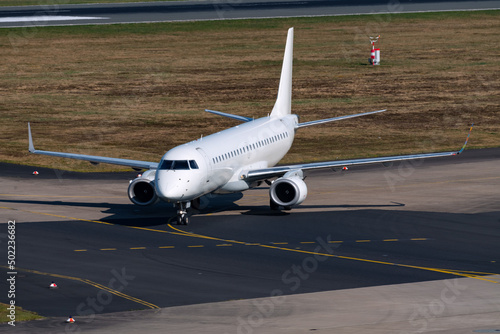 Jet plane at Airport of Cologne and Bonn Germany after landing on background runway. Aircraft rolling towards terminal on a taxi way. Frontal view of white aircraft with two turbine engines.