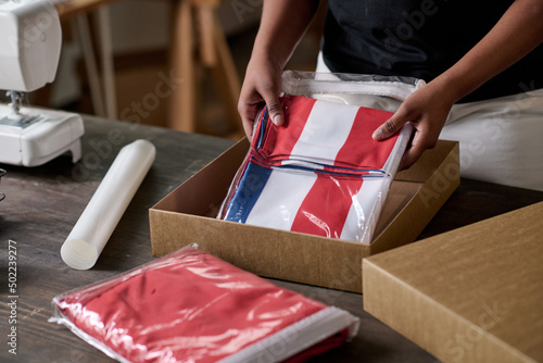 Hands of young black woman putting folded handmade USA flag into box while packing it to send to American veterans of labor