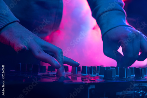 Close-up image in neon lights. Male hands turning sounds on professional dj mixer. Creative soundmaker