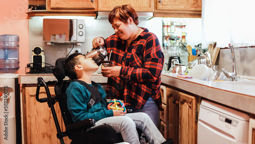 Bild auf Leinwand Latin mother taking care of son with disability on wheelchair inside home kitche