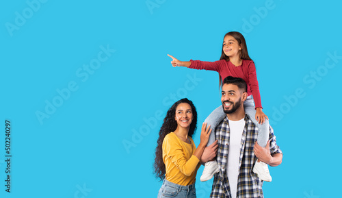 Arabic Girl Pointing Finger Sitting On Father's Shoulders, Blue Background