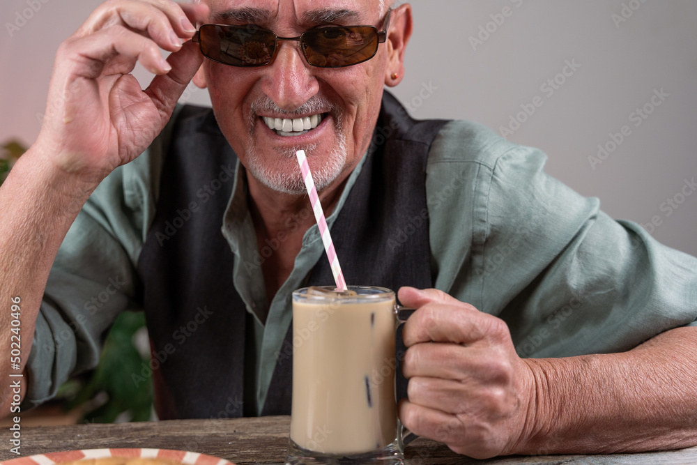 casual dressed mature man with sunglasses sitting at a table drinking iced coffee casual dressed mature man with sunglasses sitting at a table drinking iced coffee