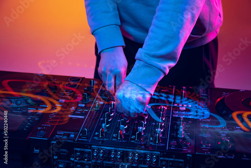 Close-up image in neon lights. Male hands turning sounds on professional dj mixer. Mixed lights effect