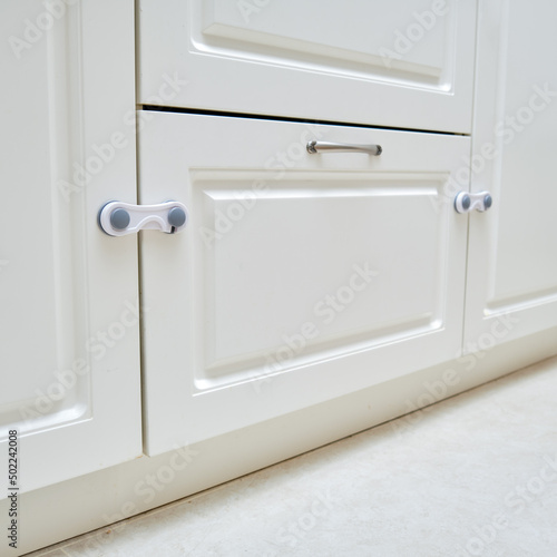 Doors of white kitchen cabinets blocked from children. Lock furniture drawers from toddler baby