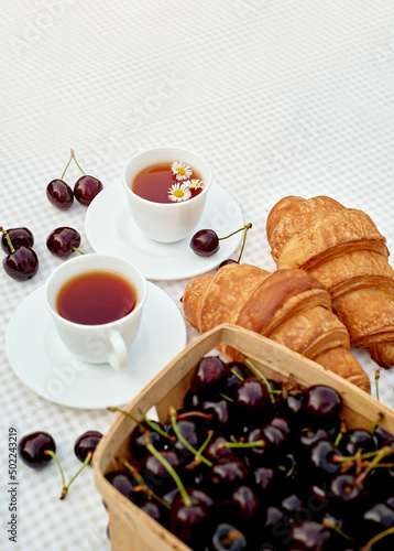 Black tea with fresh croissants and cherries on the table against white background. Flat lay, spring breakfast conceptual composition