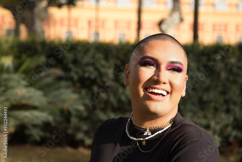 Portrait of non-binary person, young and South American, heavily make up, smiling happily, getting sun rays on face. Concept queen, lgbtq+, pride, queer. photo