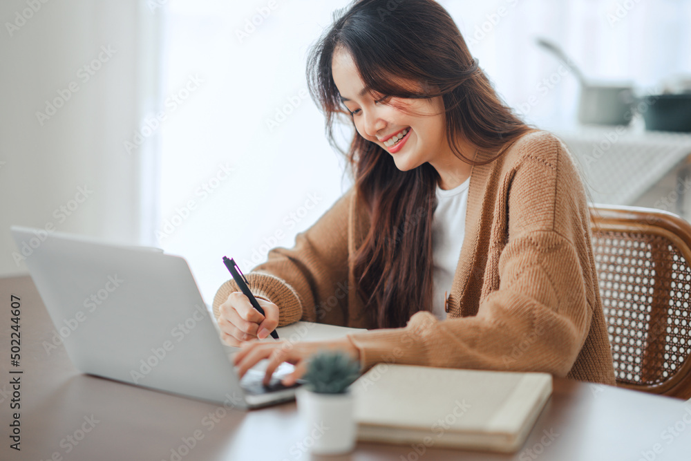 Close up happy young asian woman using laptop, writing, watching webinar, training, involved in internet lesson, motivated positive student studying online at home. education concept. Close up happy young asian woman using laptop, writing, watching webinar, training, involved in internet lesson, motivated positive student studying online at home. education concept.