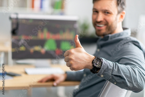 Positive mature businessman working on computer with graphs and charts on screen, showing thumb up, selective focus