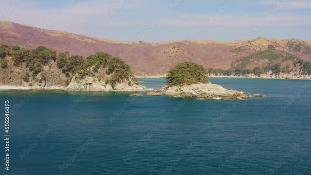 A beautiful rocky island covered with coniferous trees connected to the shore by a narrow isthmus in the Telyakovsky Bay. Sea waves crash on the shore. Beautiful rocks are covered with pine trees A beautiful rocky island covered with coniferous trees connected to the shore by a narrow isthmus in the Telyakovsky Bay. Sea waves crash on the shore. Beautiful rocks are covered with pine trees