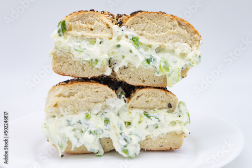 Cut in Half and Stacked New York City Style Toasted Everything Bagel filled with Scallion Cream Cheese on a White Plate