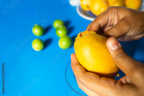 Closeup of the hand of a Latin woman peeling a mango with a blue background with jocotes and typical summer fruits in Nicaragua, Central America and Latin AmericaCloseup of the hand of a Latin woman photo