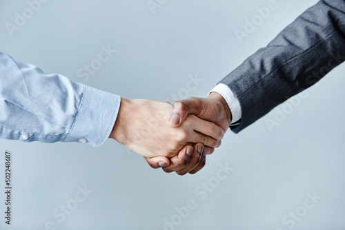 Minimal close up of two business people shaking hands against simple blue background, copy space