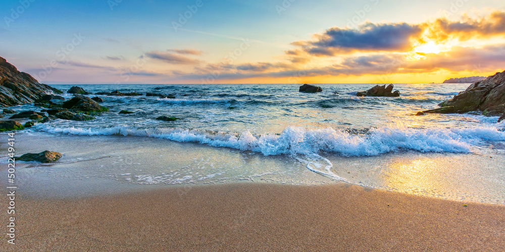 empty beach at sunrise. beautiful landscape at the sea. waves washing the sand and stones on the shore. clouds glowing in morning light. calm summer vacation and travel destination concept