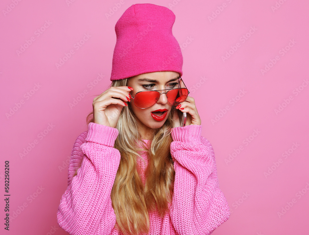 smiling girl talking on smartphone in pink clothes over pink background wearing pink hat pink sunglasses and pink pullover. Life style concept. smiling girl talking on smartphone in pink clothes over pink background wearing pink hat pink sunglasses and pink pullover. Life style concept.