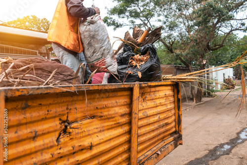 A municipal worker collecting garbage on top of a truck in a poor community in Managua, Nicaragua. Concept of solid waste management in Central America, South America and Latin America.