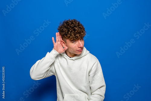 Young caucasian man wearing casual clothes smiling with hand over ear listening and hearing to rumor or gossip. deafness concept.