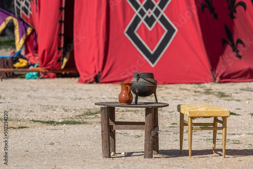 closeup of a wooden table and chair with an old cauldron and clay jug on the table as a decoration of a medieval military camp
