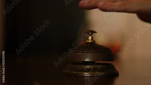 call on a old hotel bell on a wood stand. the visitor's hand calls the concierge at the hotel reception in the reception bell. at first once, then repeatedly presses the button