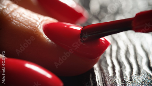 Master painting nails with bright red varnish to client closeup