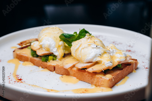 Toast with egg poached, healthy breakfast of waffles, poached egg with bacon and arugula. Brioche sandwich