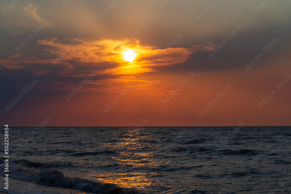 A sunset on the beach in summer. Sea and eveninig sky with clouds. Colorful sunset sky on the seashore. Amazing sea sunset, sun, waves, clouds. Beautiful cloudy landscape over the sea