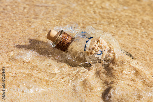 Strandgut, alte leere Flasche an einem Strand im Sand umspült vom Wasser an der Küste. photo