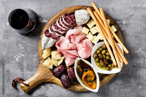 Italian snack and antipasti on a tray and red wine: prosciutto, salami, sun-dried tomatoes, olives, cheese, grissini and dates. Summer snack