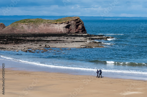 A couple walking on an empty sandy beach in East Lothian scotland