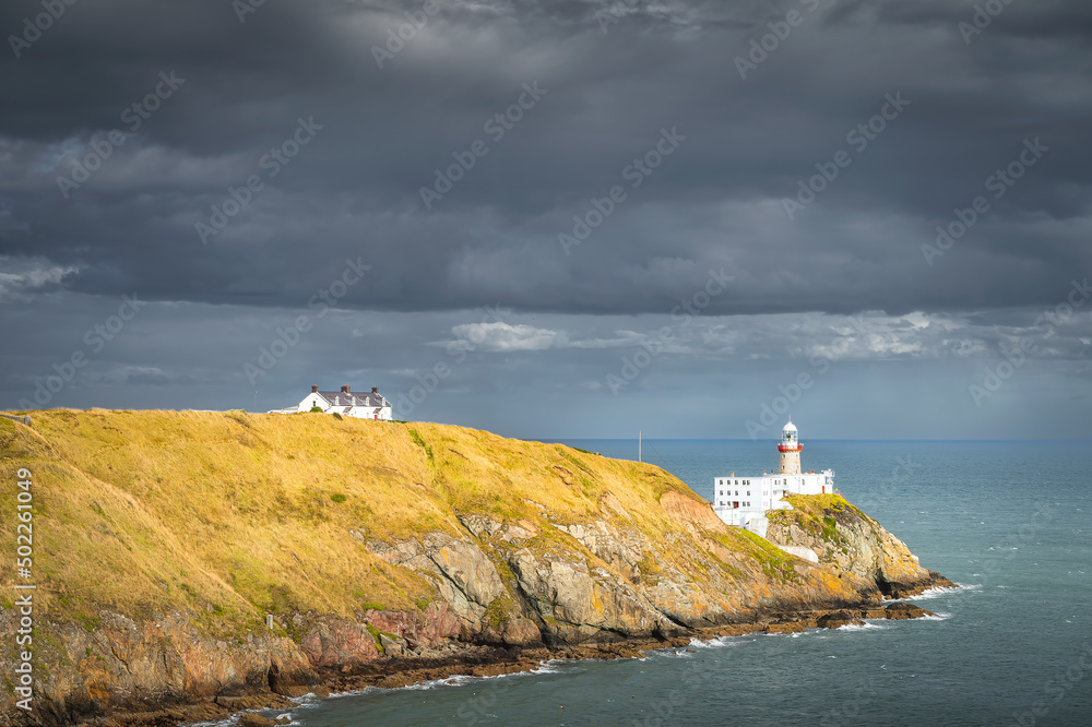 Dark storm clouds and Baily Lighthouse illuminated by fleeting sunlight in Howth peninsula, Dublin, Ireland