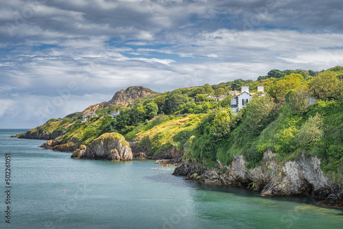 Turquoise coloured Irish Sea, small rocky islands, Howth cliff walk with some residential houses and lush green vegetation, Dublin, Ireland photo
