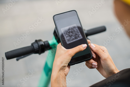 Woman scan QR code by smart phone to unlock and rent electric push scooter on street. Eco friendly transportation in city. Close up. Modern technologies.