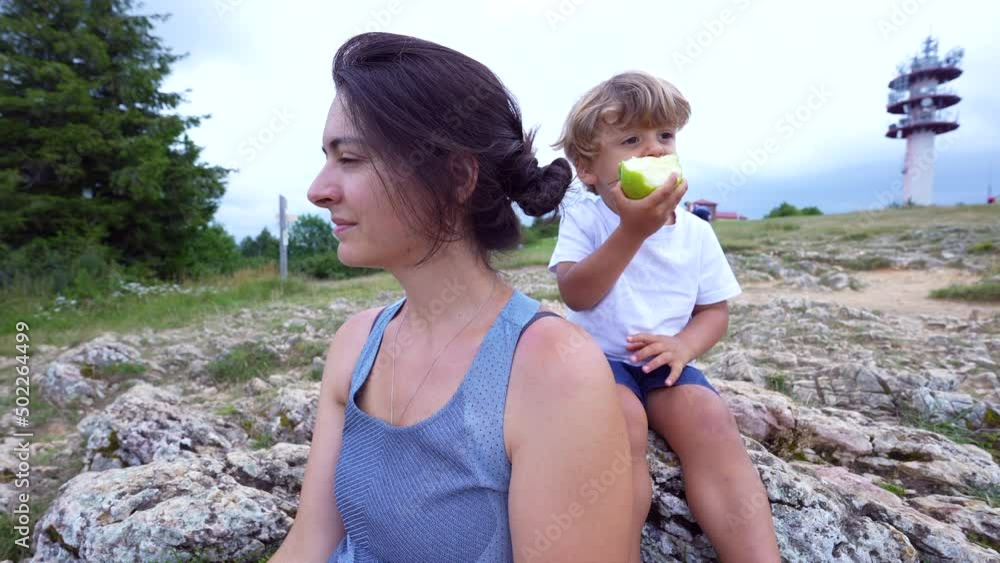 Mother contemplating nature looking at horizon next with her lttle boy toddler son eating green apple Mother contemplating nature looking at horizon next with her lttle boy toddler son eating green apple