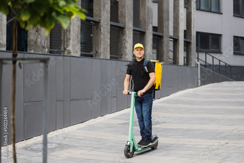 Man courier on scooter in town streets with a hot food delivery from takeaways and restaurants to home, express food delivery and shopping online concept. Delivery food by scooter. photo