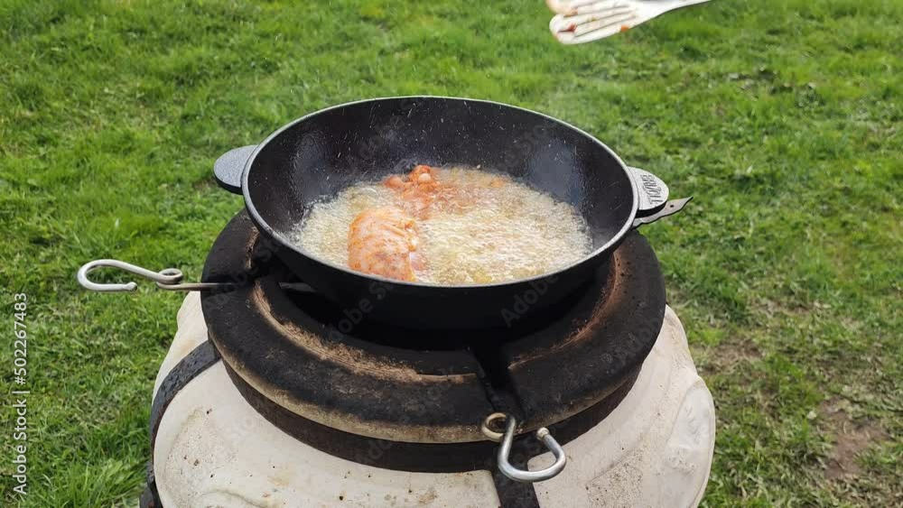 Cooking grilled chicken in a wok over an open fire. Girl cook puts food in boiling oil. 27 April 2022, Minsk, Belarus Cooking grilled chicken in a wok over an open fire. Girl cook puts food in boiling oil. 27 April 2022, Minsk, Belarus