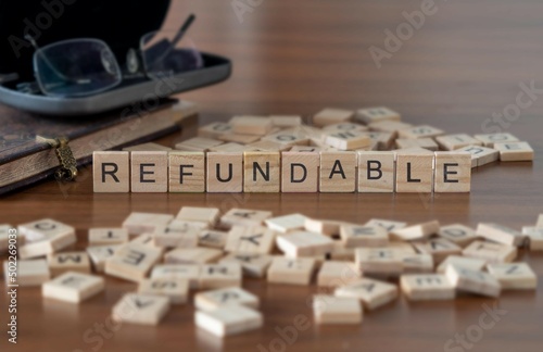 refundable word or concept represented by wooden letter tiles on a wooden table with glasses and a book photo