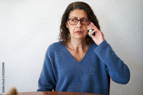 Senior phone fraud concept. Mature woman distrusting phone call photo