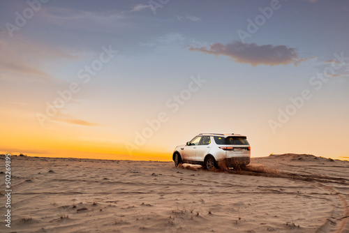 White SUV in the desert at sunset. Off road Test drive. A car in the desert quickly rides through the mud with clouds of dust from under the wheels © Natalia Shmatova