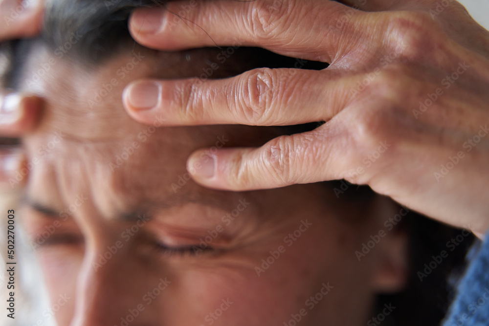 Wrinkled hands touch head of woman with headache
