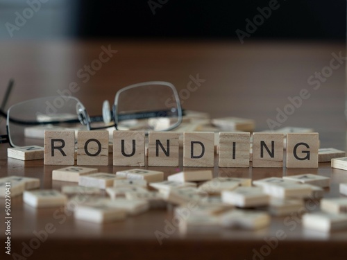 rounding word or concept represented by wooden letter tiles on a wooden table with glasses and a book photo