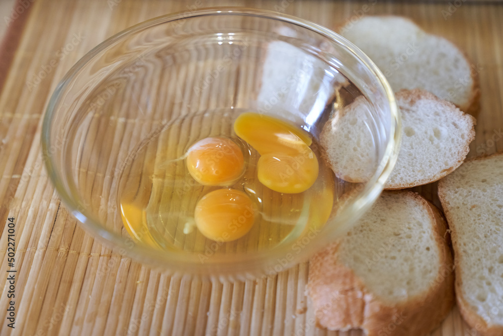 Three raw eggs in a clear glass bowl on the kitchen table with white bread. Step-by-step cooking of eggs for breakfast. High quality photo Three raw eggs in a clear glass bowl on the kitchen table with white bread. Step-by-step cooking of eggs for breakfast. High quality photo