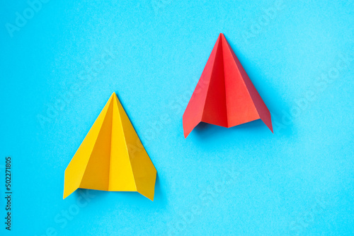 multicolored paper planes on a blue background. The concept of leadership, teamwork and courage. © Alena