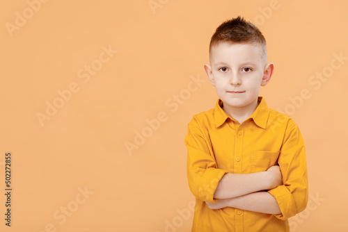 Photo of attractive cheerful nice school boy standing with his arms crossed in front of camera while isolated on yellow background. High quality photo
