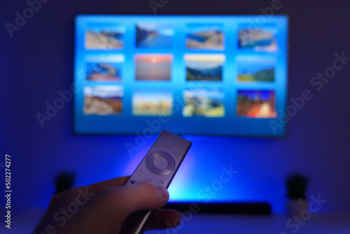 A man holding remote control and pointing out the smart TV. Screen and device highlighted in blue. Modern living room equipped with new technology like smart TV, sound bar.