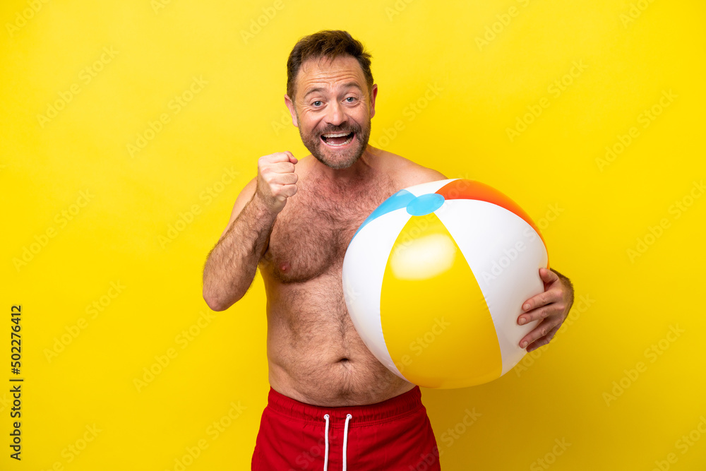 Middle age caucasian man holding beach ball isolated on yellow background celebrating a victory in winner position