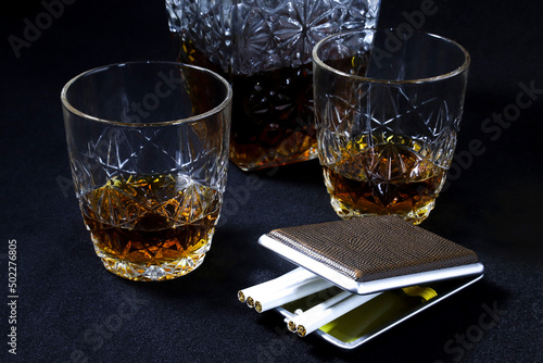 Decanter and glasses with brandy and a cigarette case with cigarettes on a black background. Close-up photo