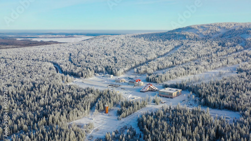 Top view of ski resort at foot of mountain. Footage. Secluded ski resort at foot of hill with ski slopes is popular in winter season. Clear sunny day on ski slopes of winter resort photo